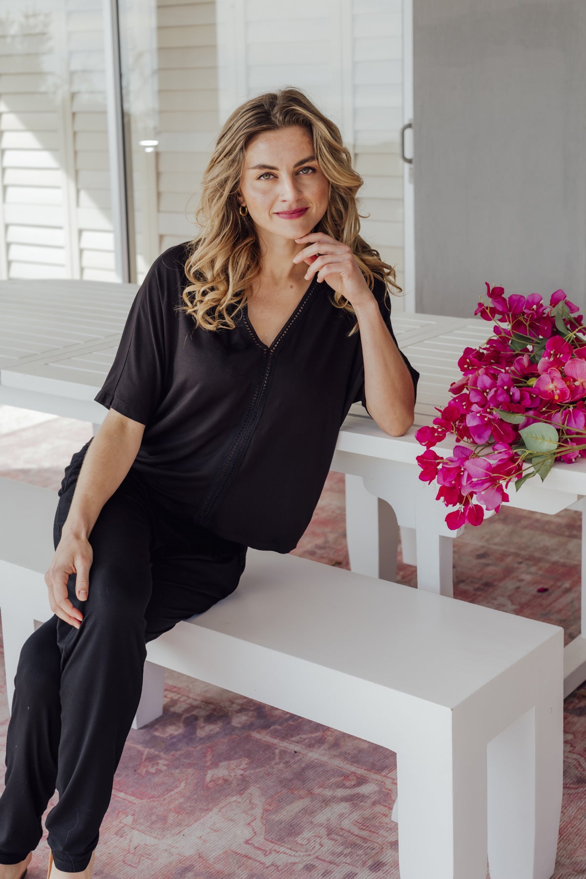 Woman in black outfit sitting on a white bench with pink flowers in the background