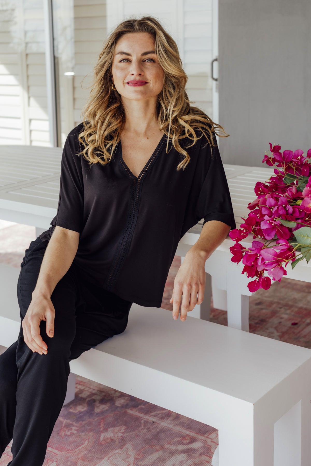 Woman in black outfit sitting on a white bench with pink flowers in the background