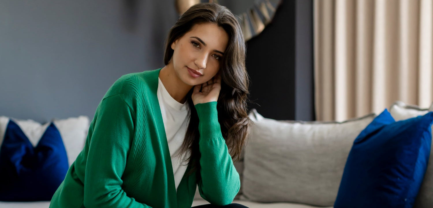Woman in a green cardigan sitting on a couch in a living room.
